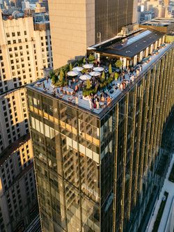 Rooftop event space in Manhattan with seating areas, umbrellas, and people overlooking the city skyline.