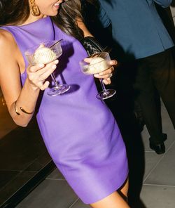 Woman in purple dress holding two glasses with desserts at a rooftop event space in NYC.