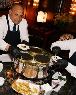 Servers serving caviar from large metal containers with side dishes and condiments on a table at Le Jardin sur Madison.