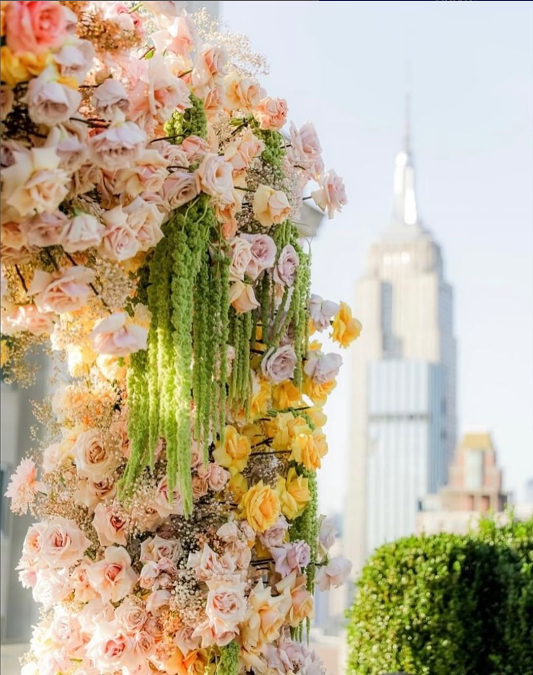 A floral arch adorned with roses and greenery, set against the Manhattan skyline, highlighting the rooftop view.
