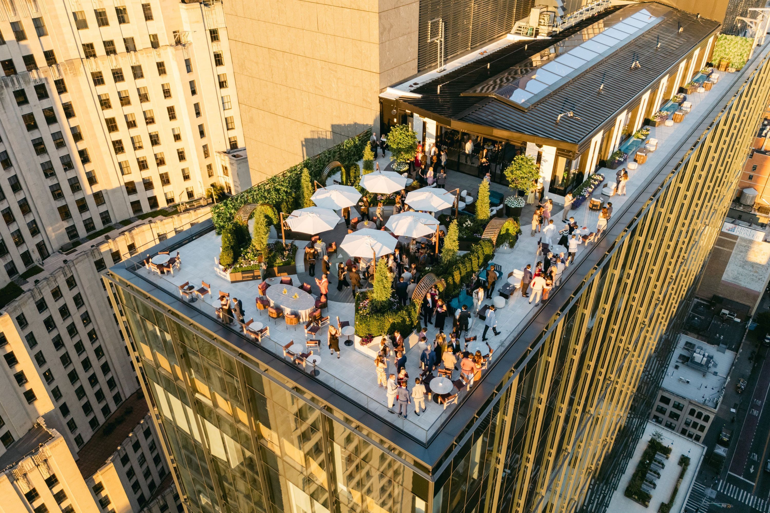 A bustling rooftop event space featuring elegant seating, vibrant greenery, and stunning views of Manhattan.