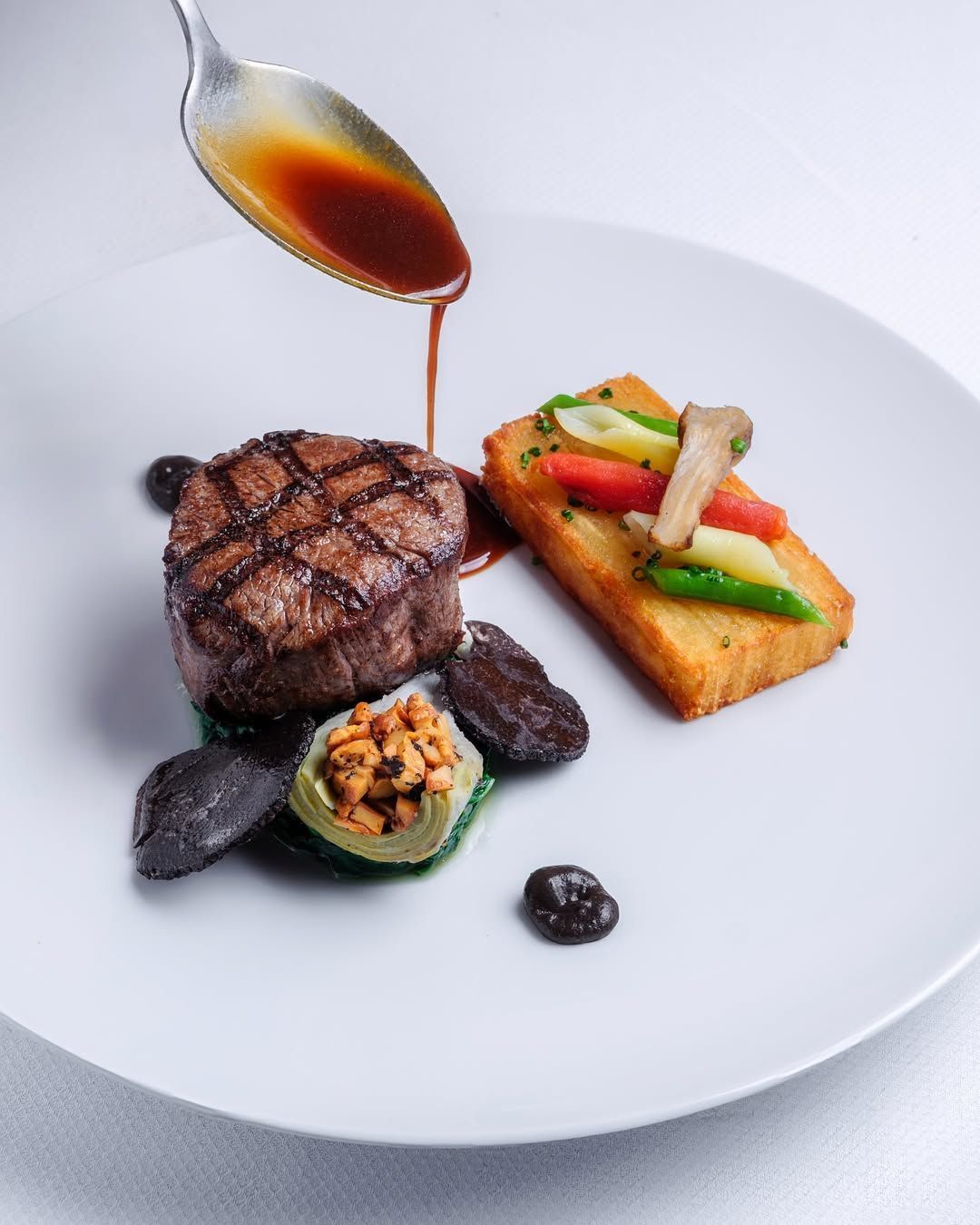 A gourmet dish featuring a grilled meat tenderloin, garnished with vegetables and sauce.