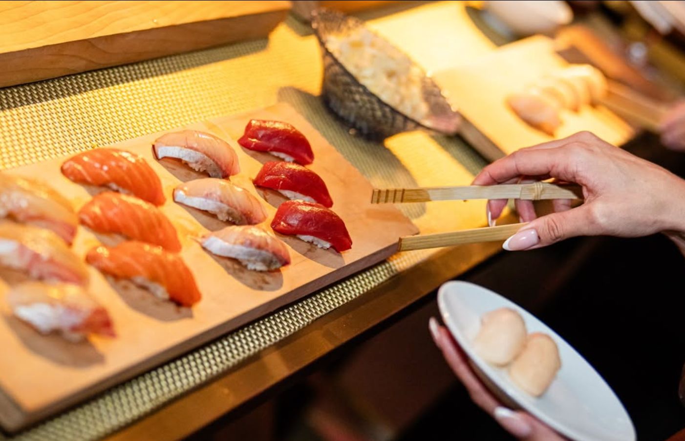 A selection of sushi displayed on a wooden platter, with a hand using chopsticks to pick up sushi.